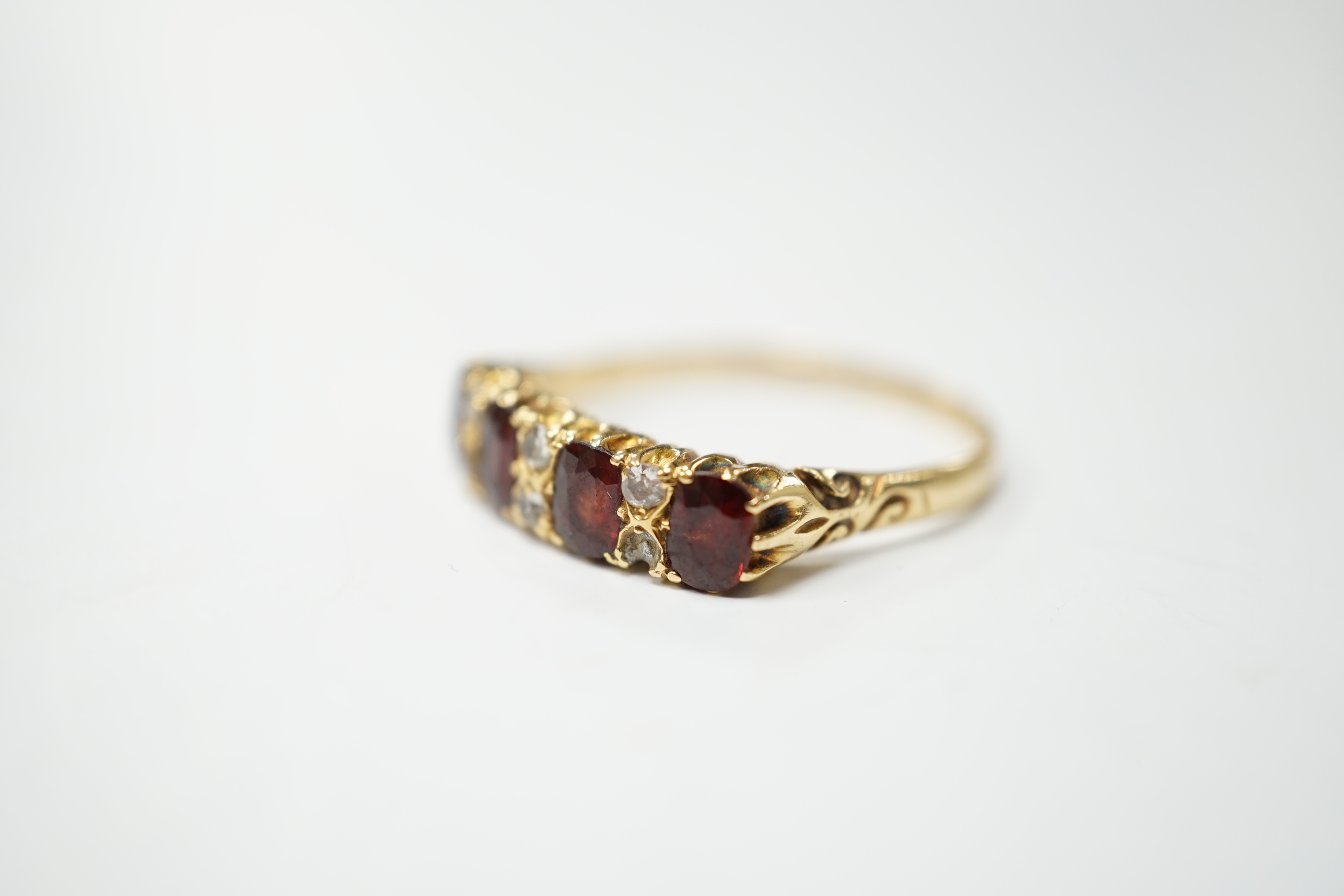 An Edwardian 18ct gold and four stone garnet set half hoop ring, with diamond chip spacers, size R, gross weight 3.6 grams.